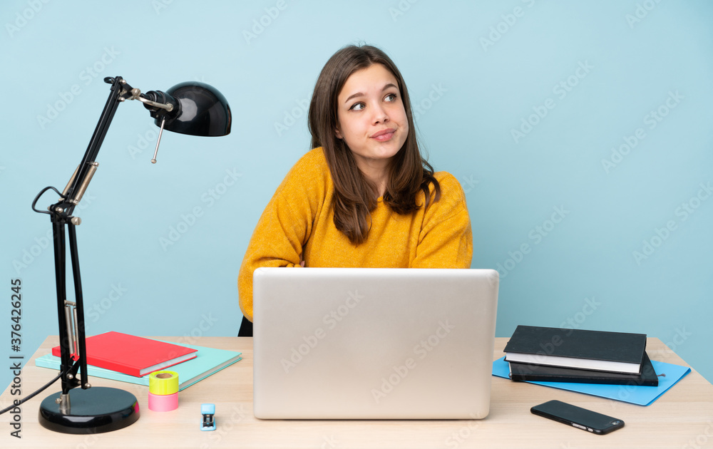 Student girl studying in her house isolated on blue background making doubts gesture while lifting the shoulders