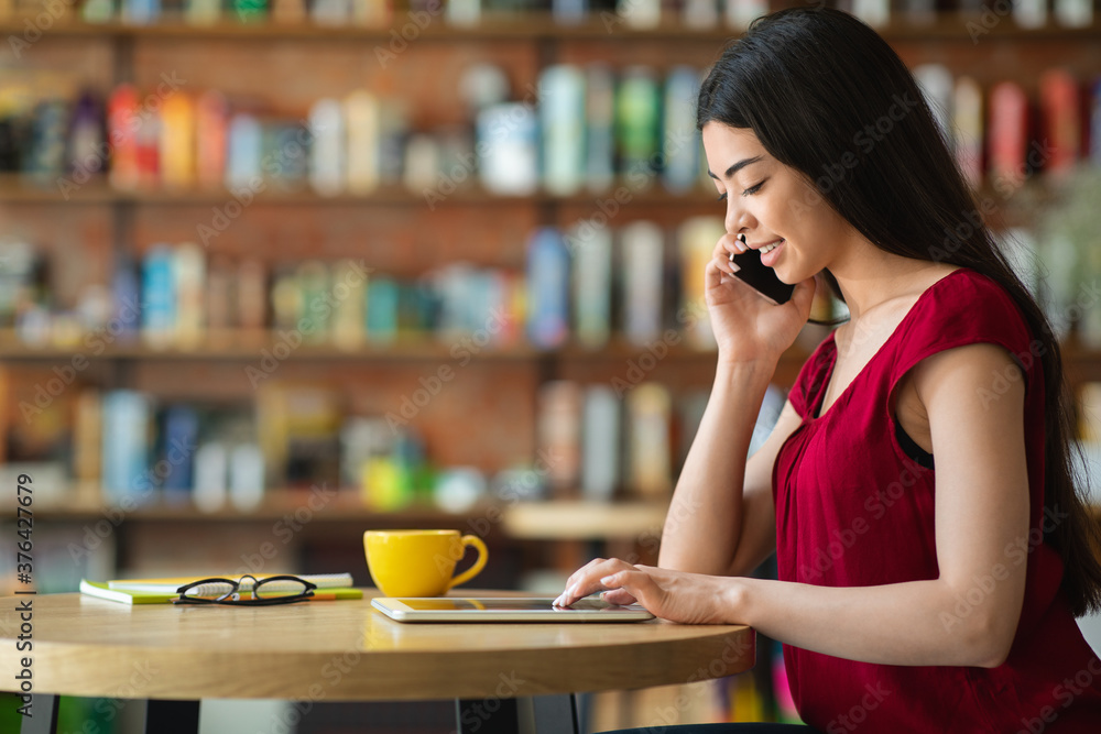 Asian female entrepreneur talking on cellphone in cafe and using digital tablet Asian female entrepreneur talking on cellphone in cafe and using digital tablet
