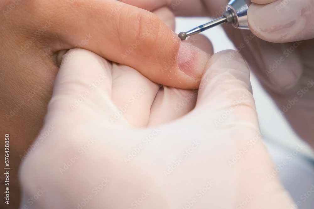 Woman manicurist is removing cuticle and pterygium using apparatus, closeup view. She is doing hardware manicure in beauty salon. Hygiene and care for hands, beauty industry concept.