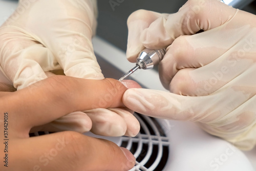 Manicurist master woman is doing hardware manicure to man, hands closeup. She is removing cuticle and pterygium on nail using electric apparatus. Hygiene and care for hands. Beauty industry concept.