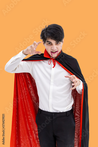 Asian man wearing Halloween costume as vampire Dracula on orange background, looking at camera