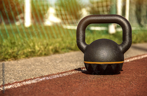 Fototapeta Naklejka Na Ścianę i Meble -  Kettlebell standing on rubber coating surface of outdoor workout ground with soccer field behind
