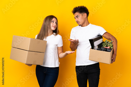 Teenager couple moving in new home among boxes isolated on blue background making unimportant gesture while lifting the shoulders