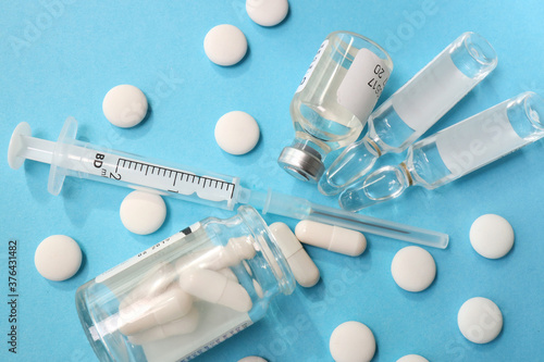 white pills and capsule are scattered on a blue background. close-up of a syringe of ampoules and a glass jar of medicine. view from above