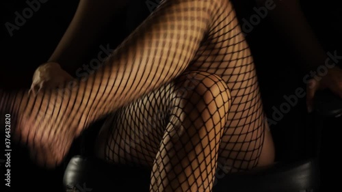 crossed female legs in fishnet stockings open and cross again on a black background photo