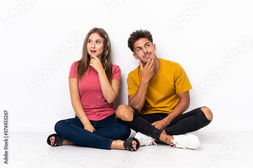 Young couple sitting on the floor isolated on white background looking up while smiling