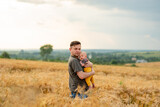A young father holds his three month old son in his arms. Filmed in a wheat field.