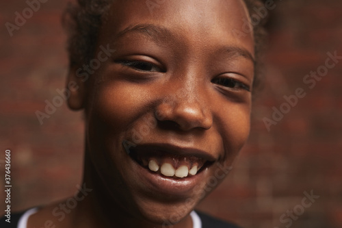 Horizontal close-up portrait of handsome African American boy standing against brick walllooking at camera smiling, copy space