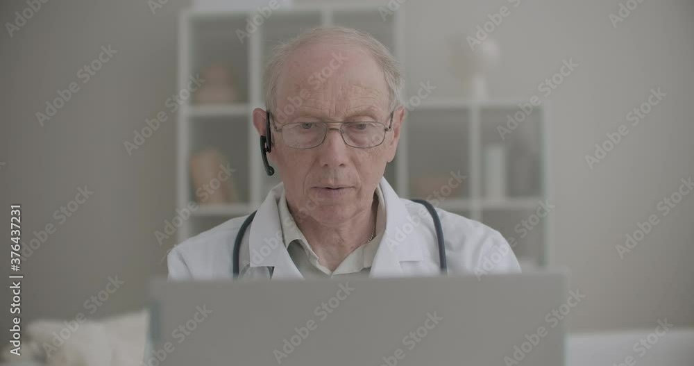 elderly professor of medicine is using laptop for online consulting of patients and intern students from his office elderly professor of medicine is using laptop for online consulting of patients and intern students from his office