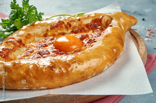 Ajarian khachapuri dish of Georgian cuisine with melted salted cheese, yolk and butter on parchment. CLose up, selective focus photo