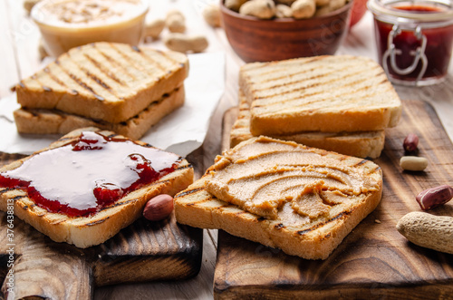 Low angle view at peanut butter and jam  sandwiches on cutting board with toasts aside. Healthy eating concept