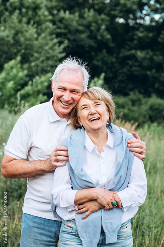 mature couple is walking with dog in park. Elderly couple resting in nature with a dog. Full-length portrait of an elderly man and woman in white shirts and jeans. Stylish and modern grandparents.