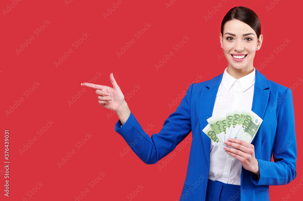 Business woman holding money and gesturing with finger and showing away, caucasian female wearing blue suit with cash, happy girl touch euro banknotes on red isolated background Business woman holding money and gesturing with finger and showing away, caucasian female wearing blue suit with cash, happy girl touch euro banknotes on red isolated background