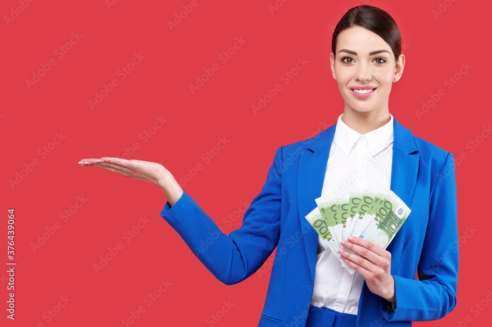 Business woman holding money and showing product, caucasian female wearing blue suit with cash, smiling girl touch euro banknotes on red isolated background Business woman holding money and showing product, caucasian female wearing blue suit with cash, smiling girl touch euro banknotes on red isolated background