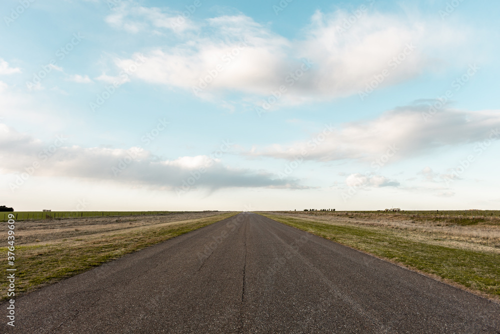 Empty asphalt road in rural zone. Beautiful sky with soft clouds at sunset.