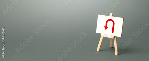 Easel with red arrow turning back. Tactical retreat for redeployment. Avoiding problems, reducing risks. Uncertainty, lack of purpose. Low discipline. Change plans, circumstances. Finding another way. photo