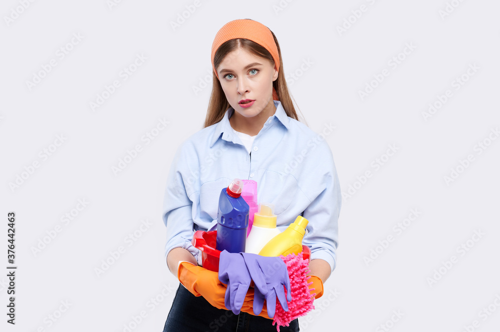 Tired caucasian housewife wearing casual clothes, latex gloves holding full red plastic basin of cleaning agent, isolated on white Tired caucasian housewife wearing casual clothes, latex gloves holding full red plastic basin of cleaning agent, isolated on white