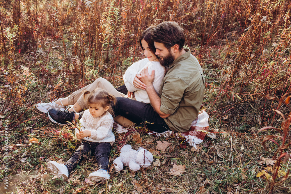 Fototapeta premium Young parents with daughter walk in autumn park, family portrait outdoors