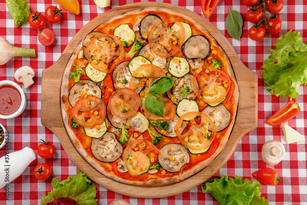 Vegetarian tasty pizza with vegetables, zucchini, eggplant, mushrooms, slices of tomato, fresh basil and tomatoes sauce on a wooden board, rustic village background, top view. Vegetarian tasty pizza with vegetables, zucchini, eggplant, mushrooms, slices of tomato, fresh basil and tomatoes sauce on a wooden board, rustic village background, top view.