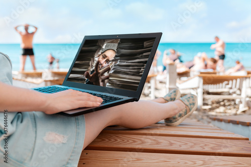 A person uses a laptop. In the background, the sea and the beach. The concept of freelancing and studying