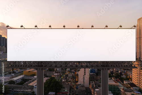 Blank white road billboard with Bangkok cityscape background at sunset. Street advertising poster, mock up, 3D rendering. Front view. The concept of marketing communication to promote or sell idea.