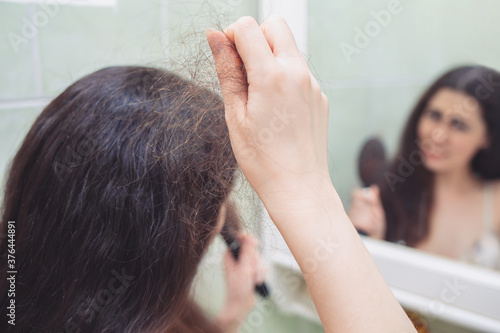 A brunette woman pulls a bunch of hair from her head. Rear view. In the background, a reflection in the mirror. The concept of hair loss