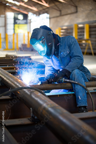 Workman in blue overalls welding some metal with sparks flying.