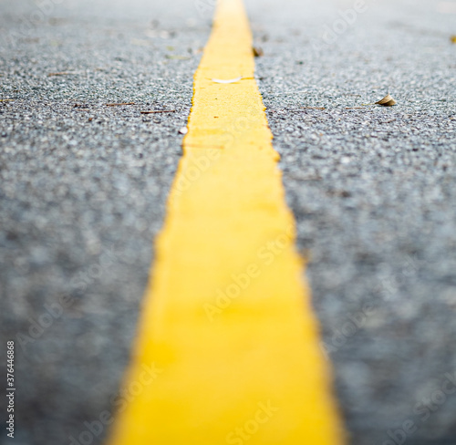 Close up view of a single yellow line on the road in soft focus, one point perspective view.