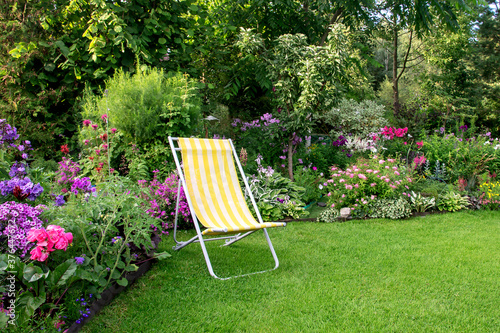 Part of the garden area with beautiful perennials, green lawn and sun lounger for relaxation. photo