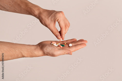 Cropped view of young guy holding pile of pills over light background, closeup