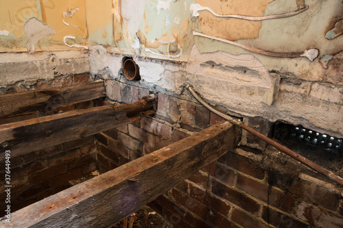 Hole in floorboards during home renovation showing into house foundations with rotting damaged joists and bare plaster walls