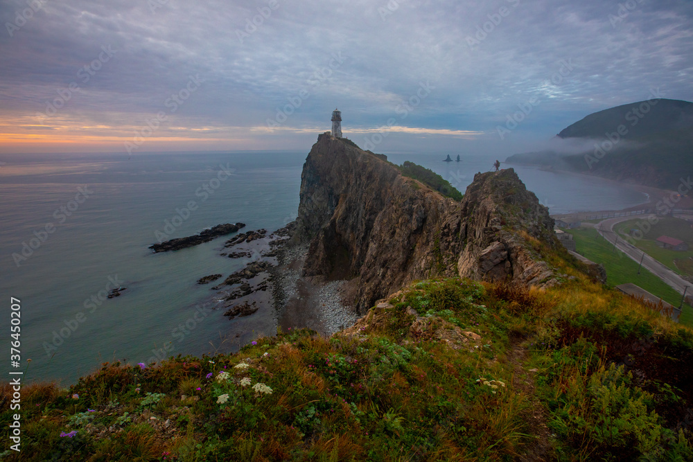 Rudny lighthouse at Cape Briner in the village of Smychka (Rudnaya Pristan), Primorsky Territory. The beautiful Rudny lighthouse stands on a sheer cliff against the backdrop of a bright dawn