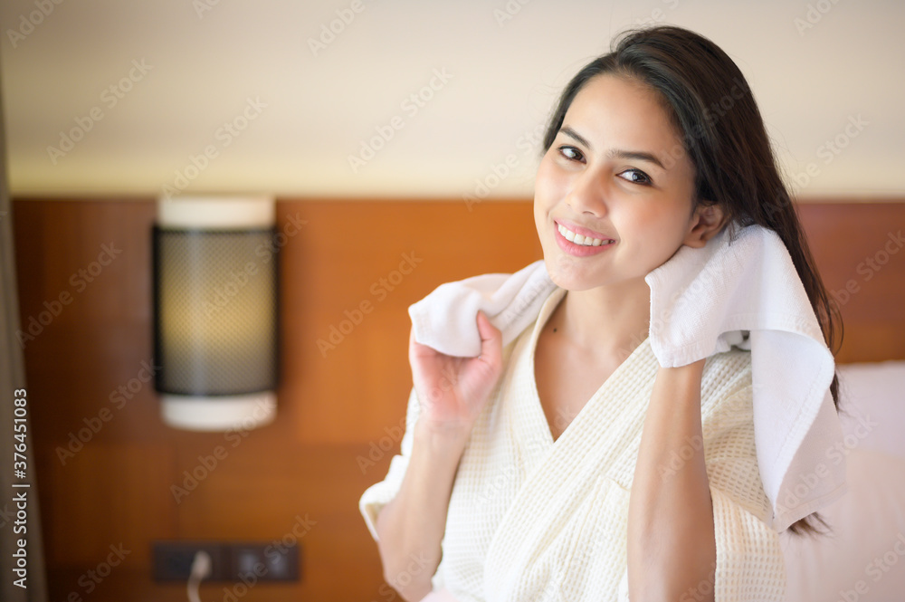 Smiling young woman wearing white bathrobe wiping her hair with towel after a shower in bedroom Smiling young woman wearing white bathrobe wiping her hair with towel after a shower in bedroom