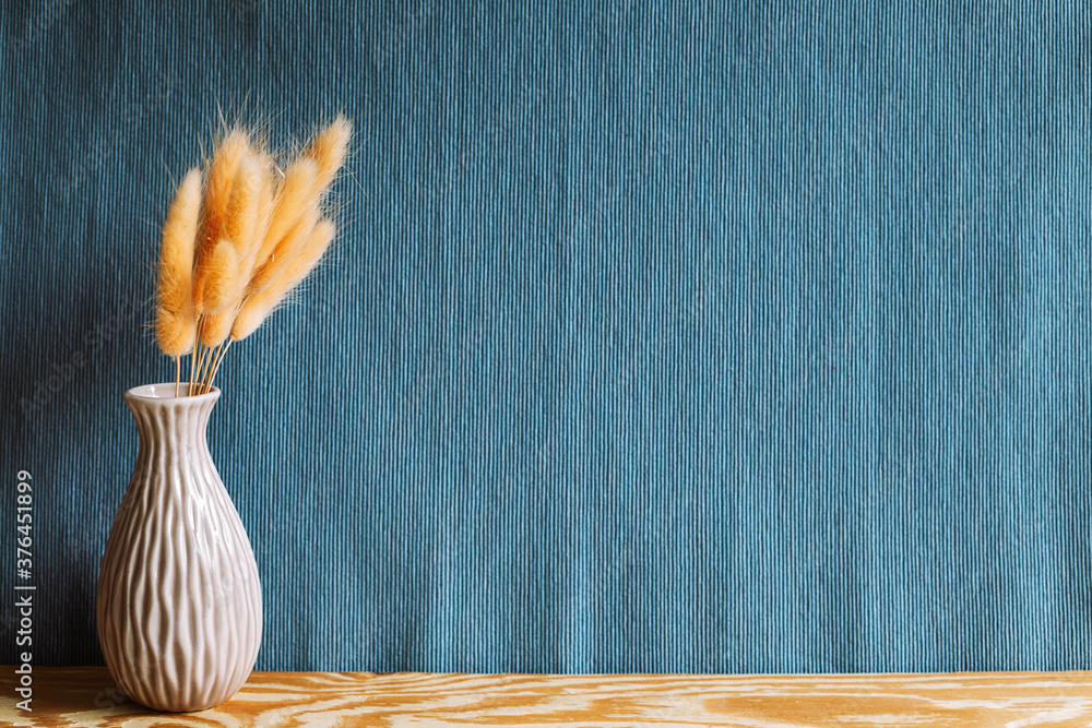 Vase of pink hares tail grass (Lagurus ovatus) dry flowers on wooden table with navy blue fabric background