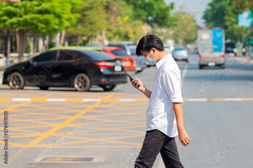 Young asian man in protective masks and looking at screen of smartphone while walking in the city street. Copy space © shine