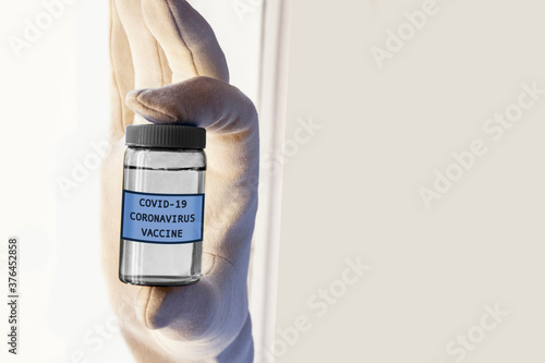 hand in a white glove holds a bottle with the inscription covid-19 vaccine. A bottle with a coronavirus vaccine in a hand, copy space for text