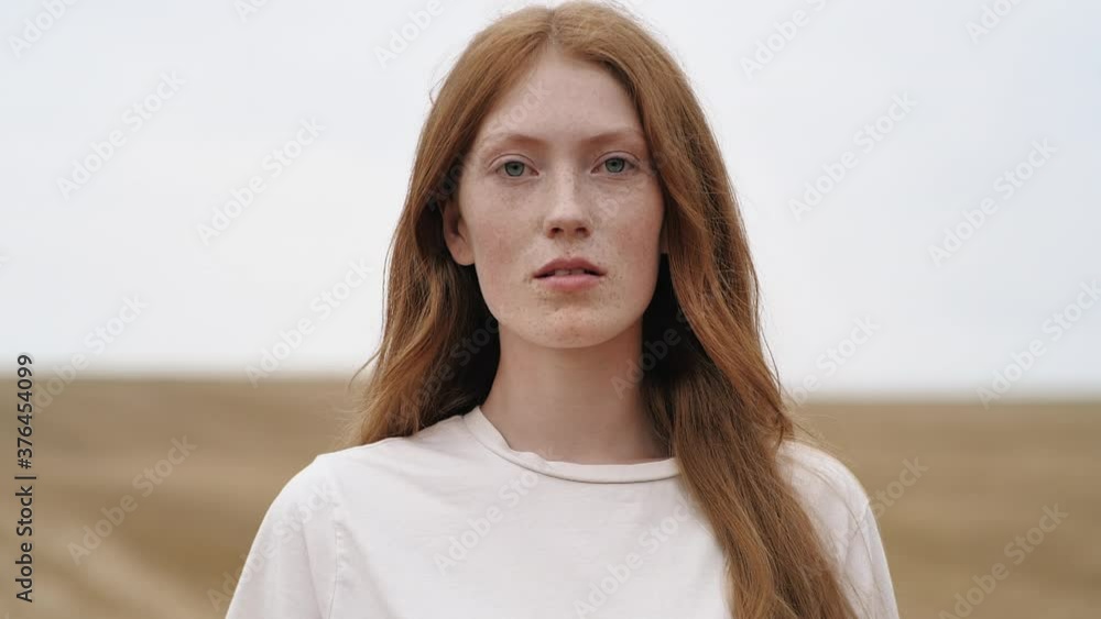 Portrait of amazing Ginger young Woman with blue Eyes, nice Freckles. Young Woman breathing fresh Air on golden Field. Wind blowing airy Red Hair. Natural Beauty. People. Liberty. Portrait of amazing Ginger young Woman with blue Eyes, nice Freckles. Young Woman breathing fresh Air on golden Field. Wind blowing airy Red Hair. Natural Beauty. People. Liberty.