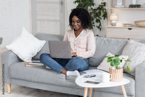 Remote Work. Joyful Black Woman Working On Laptop On Couch At Home
