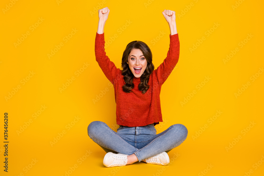 Obraz premium Full size photo of excited energetic girl sit floor legs crossed celebrate lottery win raise fists scream wear jeans jumper isolated bright shine color background
