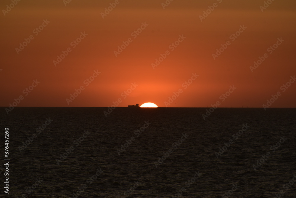 sunset on the sea, with a large cargo ship next to it