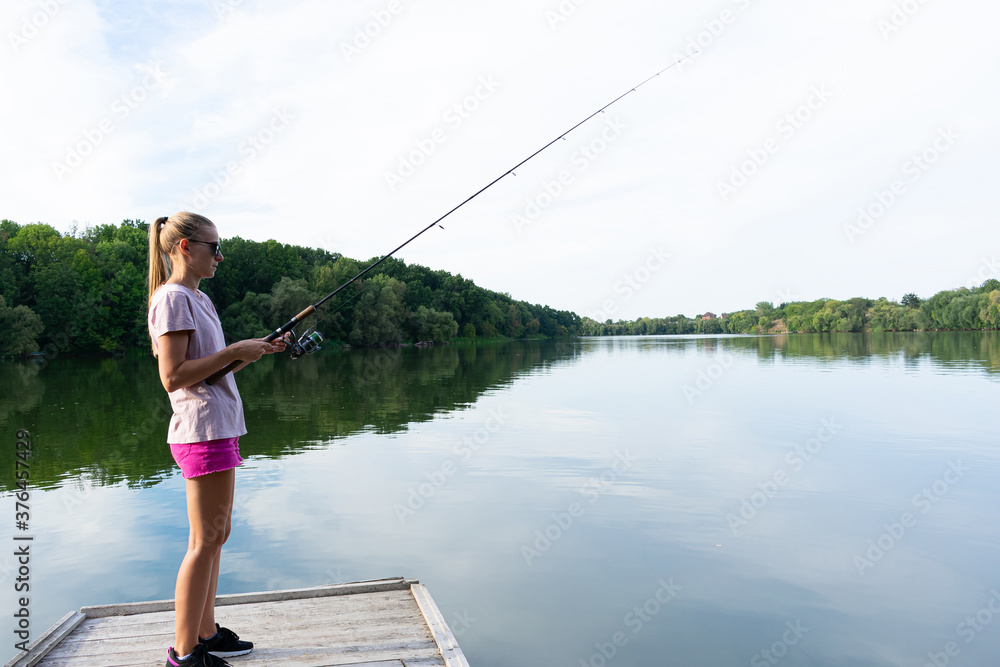 Cute woman is fishing with rod on the summer lake. Woman fishes on the river Cute woman is fishing with rod on the summer lake. Woman fishes on the river