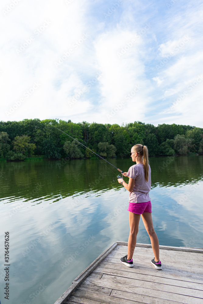 Cute woman is fishing with rod on the summer lake. Woman fishes on the river