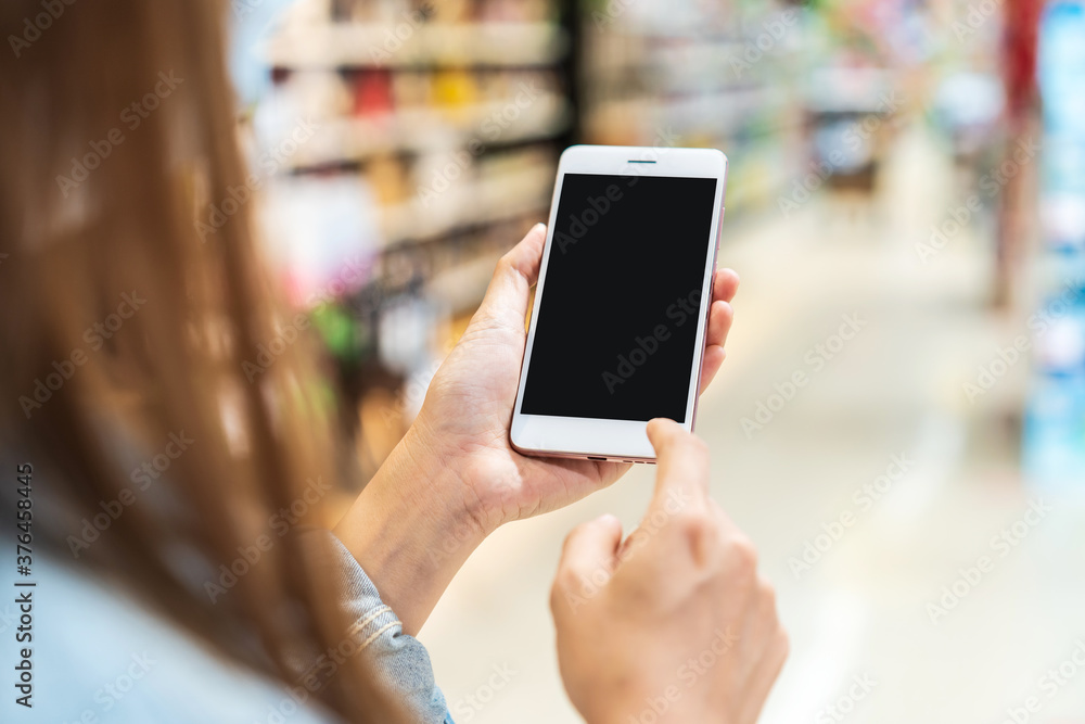 Young woman holding the empty screen smart phone while shopping in grocery store at the supermarket Young woman holding the empty screen smart phone while shopping in grocery store at the supermarket