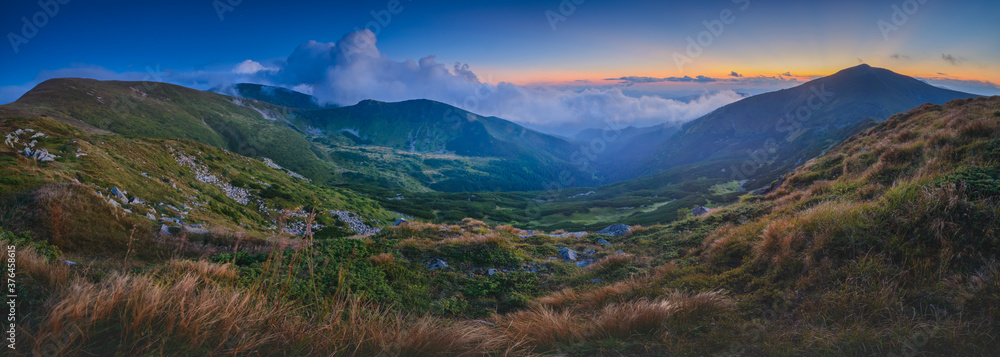 The sunset in the mountains leaves rays of light in the sky, and cumulus clouds fly over the mountains