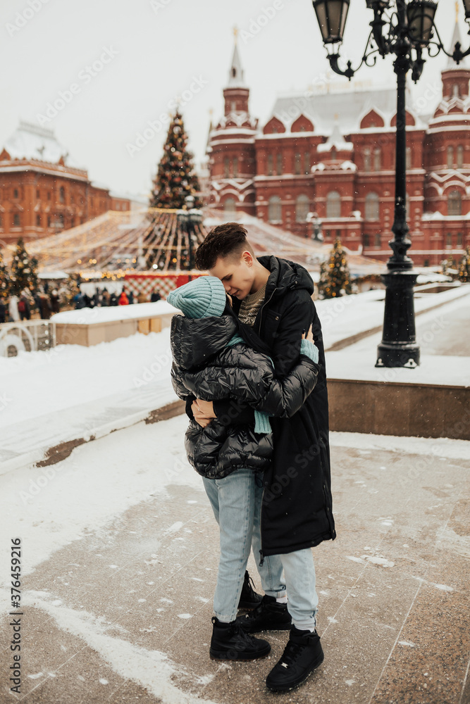 A young couple kissing in the winter against the background of the Christmas tree in the city. Love, winter holidays and people concept. Christmas vacation holidays.