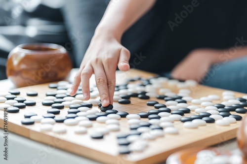 hand putting baduk black stone on wooden grid board - an ancient game also known as baduk in Korean, weiqi in Chinese and Igo in Japanese