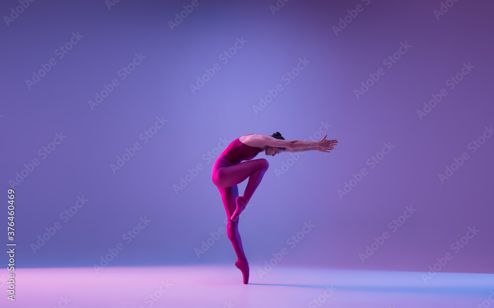 Direction. Young and graceful ballet dancer isolated on purple studio background in neon light. Art, motion, action, flexibility, inspiration concept. Flexible caucasian ballet dancer, weightless