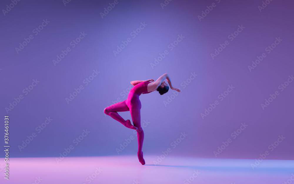 Freedom. Young and graceful ballet dancer isolated on purple studio background in neon light. Art, motion, action, flexibility, inspiration concept. Flexible caucasian ballet dancer, weightless jumps.