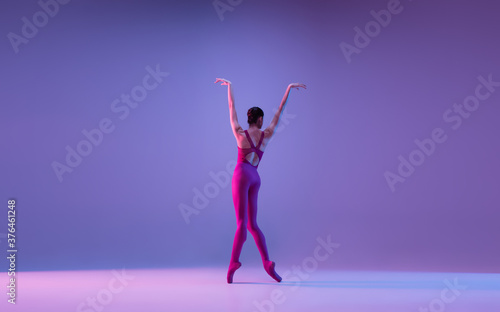 Freedom. Young and graceful ballet dancer isolated on purple studio background in neon light. Art, motion, action, flexibility, inspiration concept. Flexible caucasian ballet dancer, weightless jumps. © master1305