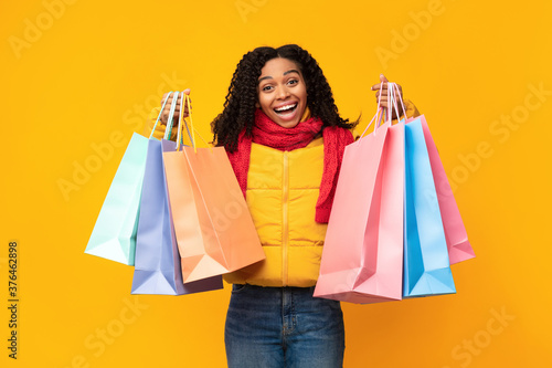 Excited Girl With Shopping Bags Posing Wearing Jacket, Yellow Background © Prostock-studio